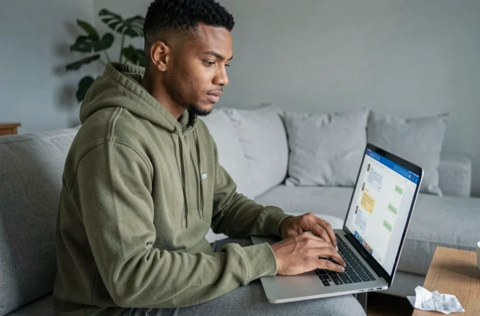Jeune personne contactant le support client en ligne sur un ordinateur portable pour récupérer un code d'enquête perdu depuis un canapé